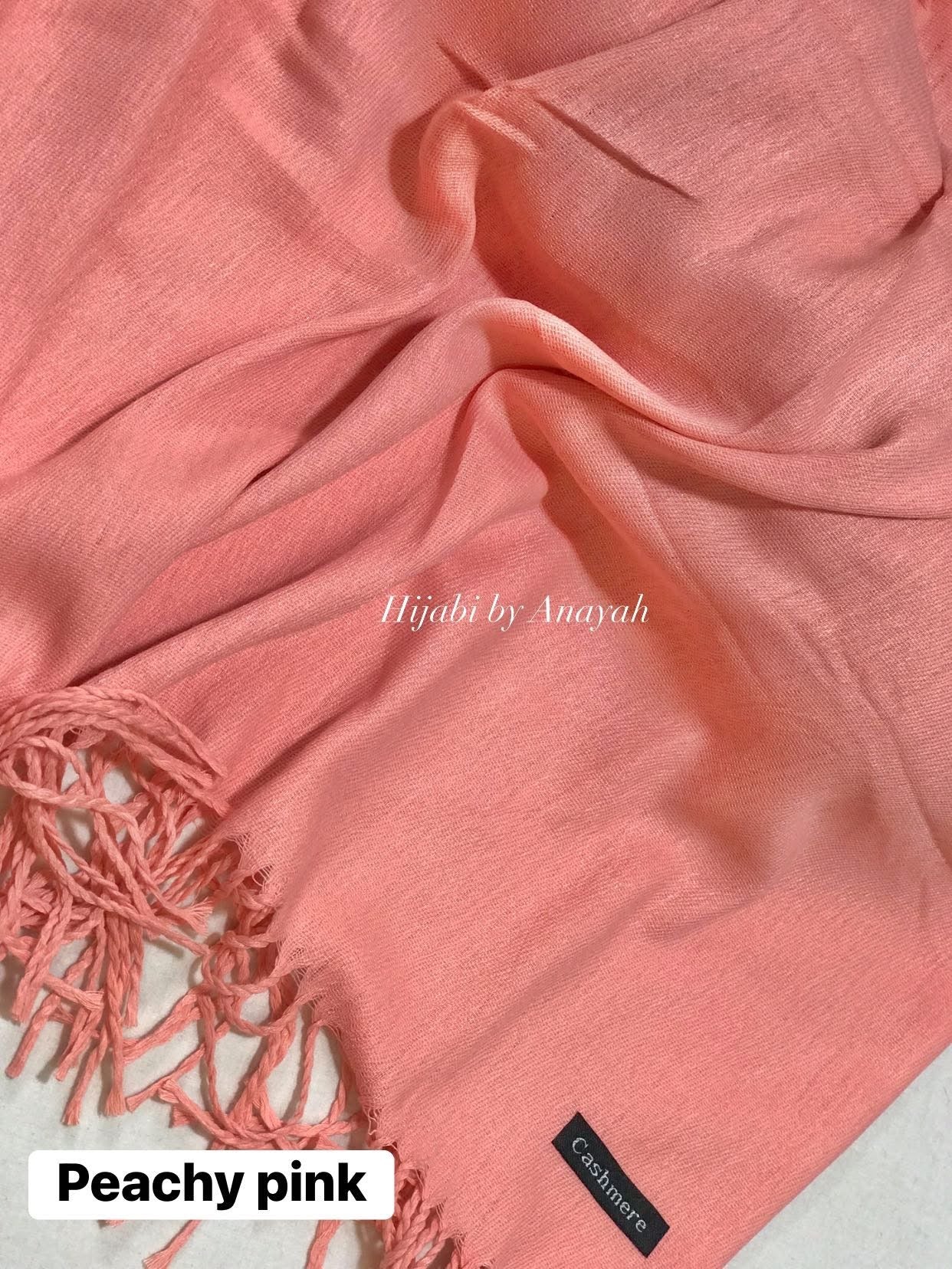 Peachy pink hijab with tassels and 'Hijabi by Anayah' branding on a light background.